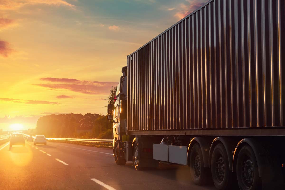 Scenic front view big long heavy semi-treailer truck with sea shipping container driving highway dramatic warm morning evening sunrise sun sky sunset. Cargo transport industry background concept